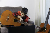 Dítě praktikuje hraní na klasickou španělskou kytaru s počítačem z domova. New Normal, Conceptual, Covid-19 Pandemic, Online učení