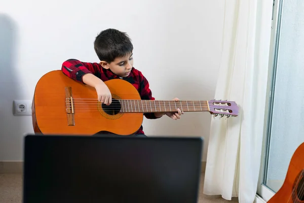 The child practices playing the classical Spanish guitar with the computer from home.  New Normal, Conceptual, Covid-19 Pandemic, Online Learning