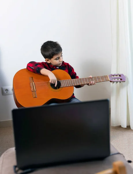 The child practices playing the classical Spanish guitar with the computer from home.  New Normal, Conceptual, Covid-19 Pandemic, Online Learning