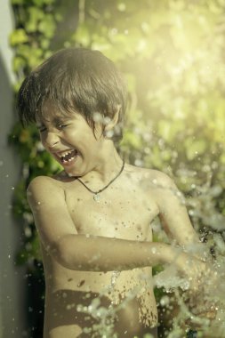 Mayo giymiş gülen çocuk gün batımında hortumla ıslanır. Yaşam tarzı kavramsal.
