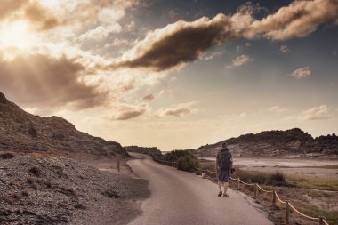 Sırt çantalı ve fotoğraf makineli turist gün batımında yolda yürüyor. Turizm kavramı, yaşam tarzı