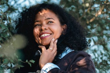 Küba kökenli güzel bir Afro-Amerikalı kadın kameraya bakıyor. Yeşil ağaçların olduğu bir ormanda. İnsanlar, yaşam tarzı, güçlü kadınlar, moda.