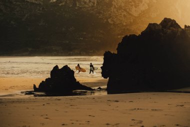Sırtı gün batımına dönük iki sörfçü Cantabria sahilinde, kuzey İspanya 'da, yaşam tarzı, seyahat, sakinlik, rahatlama, spor