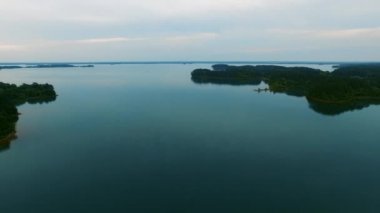 Yavaşça büyük ahşap bir iskelenin üzerinden göle doğru yürüyorlar ve göl suyunun üzerinde uçuyorlar. Bir dağ ormanı gölünde çam ağaçlarıyla birlikte turkuaz su. Mavi göl ve yeşil orman gölü havadan görünüyor.. 