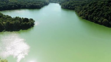 Yavaşça büyük ahşap bir iskelenin üzerinden göle doğru yürüyorlar ve göl suyunun üzerinde uçuyorlar. Bir dağ ormanı gölünde çam ağaçlarıyla birlikte turkuaz su. Mavi göl ve yeşil orman gölü havadan görünüyor.. 