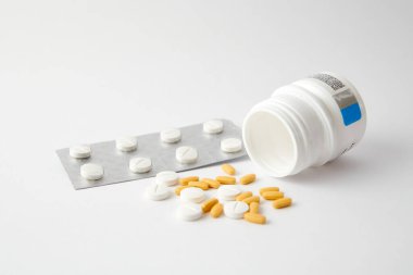 Beyaz ve sarı haplardan oluşan bir yakın çekim beyaz yüzeydeki ilaç şişesinden düşüyor.