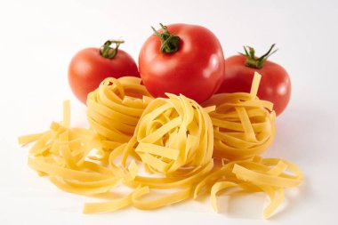 Pişmemiş makarna ve beyaz arka planda izole edilmiş taze olgun domateslerin yakın plan çekimi.