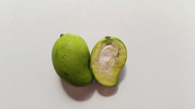 Taze, yeşil bir mangoya yakın plan, bütün ve ikiye bölünmüş, tohum ve sulu hamuru gösteren, beyaz bir arka planda izole edilmiş. Tropikal meyve, tazelik, doğal gıda, sağlıklı beslenme, organik ürün ve mutfak malzemeleri kavramı.