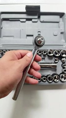 Beyaz arkaplanda izole edilmiş plastik bir kutuda düzenlenmiş soket aletli bir anahtar kullanan bir el..
