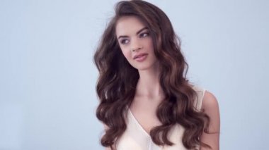 Uzun kıvırcık kahverengi saçlı güzel bir kadın. Moda modeli stüdyodaki kameraya bakıyor. Çekici esmer bir kadının yakın çekim yüzü. Saexy görünüşlü seksi bir manken. 4K görüntü. Yavaş çekim. 