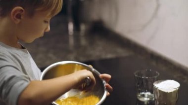Çocuk, krema yapmak için demir maskeli çırpıcıyla yumurta sarısı çırpıyor. Çocuk kurabiye yapmak için un karışımını karıştırıyor. Mutfakta yemek pişiren 8 yaşında bir çocuk. Yemek zamanı. Çocukluk kavramı.