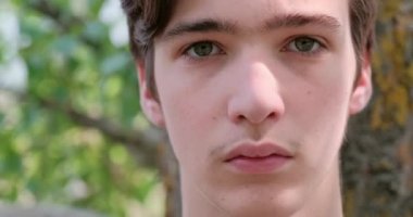 Genç üzgün adam kameraya bakıyor. Mutsuz, yalnız, genç bir delikanlı, açık havada. Hüzünlü bakışları olan yakışıklı bir adamın yakın çekim yüzü. Hüsrana uğramış genç yüzü, dışarıda.