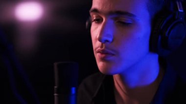 Profesyonel bir müzisyenin, kulaklıklı bir şekilde şarkı söylerken çekilmiş sinematik görüntüleri. Şarkıcı bestesini bir müzik stüdyosunda kaydediyor. Genç Çocuk mikrofona şarkı söylüyor.. 