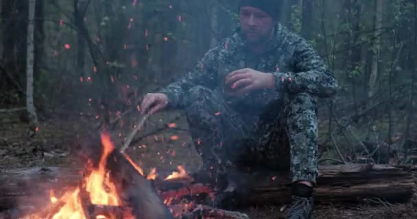 男は森の中で火の近くで熱いお茶を飲む 人間は森林火災を見て 夏には自然の中でお茶を飲みます 夕暮れ時にはコーヒーを片手に一人旅の疲れを癒す — ストック動画