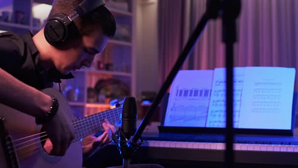 音乐家戴着耳机在音乐工作室里用专业的音频话筒记录他的作品 年轻人在他的房间里弹吉他 少年男孩弹奏一种乐器 — 图库视频影像