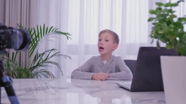 Çocuk blogcu video bloğunu evde kaydediyor. Çocuk video blogunu kaydediyor. Beyaz çocuk blog kanalı için bir video kameranın önünde konuşuyor. Küçük 8 yıllık vlogger kayıtları akıllı telefon kullanarak çevrimiçi yayınlanıyor