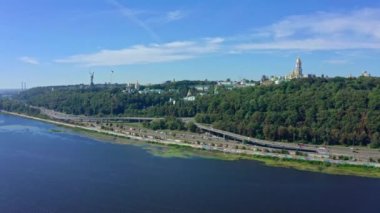 İnsansız hava aracı, Pechersk Lavra, Anavatan heykeli ve şehir merkezi manzaralı Dnipro nehrinin üzerinden havalanıyor. 2020 yazında Kiev şehrinin sinematik kuş bakışı görüntüsü.