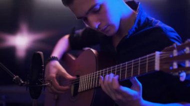 Genç, odasında gitar çalıyor. Genç adam bir müzik aleti çalıyor. Müzisyen bestesini profesyonel mikrofon kullanarak bir müzik stüdyosunda kaydeder. Profesyonel ışıklandırma 