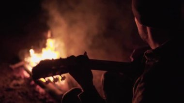 İnsan doğada kamp ateşinin yanında gitar çalıyor. Ateşin yanında doğada hafta sonu. Yetişkin adam geceleri ateşin yanındaki ormanda dinleniyor..