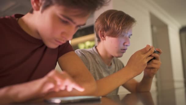 十几岁的男孩在家里带着智能手机 两个男孩子用手机在社交网络上消磨时光 白人青少年使用手机玩游戏 有电话 近视的年轻人 — 图库视频影像