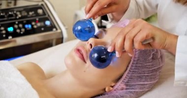 Güzellik uzmanı mavi taşakları kullanarak yüz masajı yapıyor. Yüz bakımı için kozmetik işlemleri yapan bir kaplıcadaki kadın. Kız yüz masajı yaptırıyor. Kozmetik uzmanı yüz masajı yapıyor. 