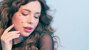 Yüzünde kırmızı kalpler olan güzel bir kız. Rüzgarda savrulan uzun saçlı güzel bir genç kadın. Model stüdyodaki kameraya bakar. Çekici bir sarışının yakın plan yüzü. Yavaş çekim