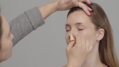 Makyaj sanatçısı ya da stilist, kadın modelin yüzüne ıslak sünger kullanarak temel oluşturur. Yüze kozmetik kapatıcı taban uygulaması. Profesyonel makyaj. Makyaj hocası sınıfı.  