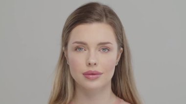 Güzel genç kız profesyonel makyajdan sonra kameraya bakar. Model kamera önünde poz verir. Güzel makyajlı çekici bir kız. Uzun saçlı beyaz bir mankenin yakın plan yüzü..