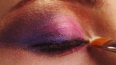 Makyaj sanatçısı göz kapağına makyaj yapar, yakın plan. Makyaj sanatçısı makyaj fırçasıyla parlak bir göz farı sürüyor. Profesyonel makyaj yüksek lisansı. Yavaş çekim sinemasal çekim. 