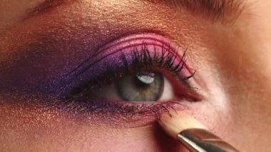 Makyaj sanatçısı göz kapağına makyaj yapar, yakın plan. Makyaj sanatçısı makyaj fırçasıyla parlak bir göz farı sürüyor. Profesyonel makyaj yüksek lisansı. Yavaş çekim sinemasal çekim. 