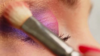 Makyaj sanatçısı göz kapağına makyaj yapar, yakın plan. Makyöz makyaj fırçasıyla parlak bir göz farı sürüyor. Profesyonel makyaj hocası sınıfı. Yavaş çekim sinemasal çekim. 
