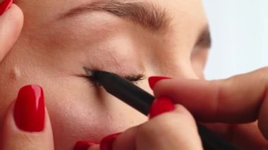 Yakın çekim, kadın modelin gözlerine siyah oklar çizen stilist. Üst göz kapağında siyah kozmetik kalem kullanan bir kadın. Profesyonel makyaj. Mua yapıyorum. Gerçek zamanlı..