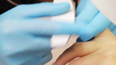 Tırnak törpüsü. Manikürcü tırnakların şeklini özel bir tırnak törpüsüyle dosyalar, görüntüyü kapat. Manikürcü tırnak törpüsüyle tırnakları şekillendiriyor. Güzellik salonunda tırnak bakımı. Yakın çekim.