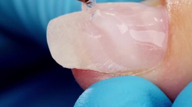 Kapatın. Tırnak uzatma servisi. Manikürcü, manikür için profesyonel aletlerle manikür jölesi uzatıyor. Uzman, müşterinin tırnağını berrak jelle kaplıyor. 