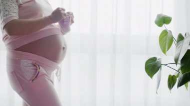Hamile bir kadın çocuğuna bakarken kendini mutlu hissediyor. Genç yaşta hamile bir anne karnında bebeği tutuyor. Kadın hamilelik konsepti ve doğum öncesi bakım ve Yavaş çekim 4K video.