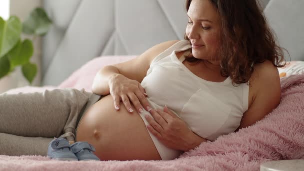 妊娠中の女性は子供の世話をしながら家で幸せを感じています 妊婦のお腹に赤ちゃんを抱いている母親を期待している 女性の妊娠の概念と産前ケア スローモーション4Kビデオ — ストック動画