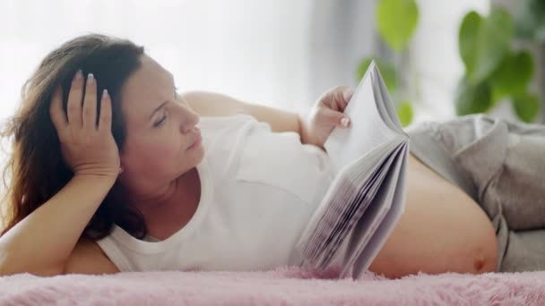 Ευτυχισμένη Έγκυος Γυναίκα Περιμένει Ένα Μωρό Ξαπλωμένο Στον Καναπέ Διαβάζοντας — Αρχείο Βίντεο