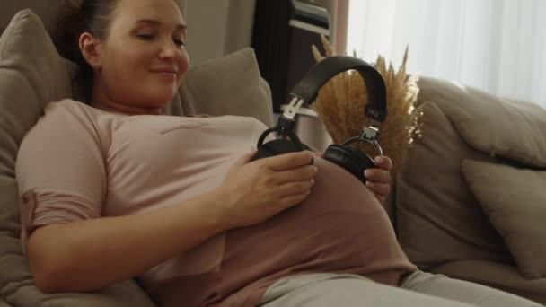 여자는 헤드폰으로 음악을 듣는다 아기를 행복하게 기다리고 있습니다 여자는 집에서 — 비디오