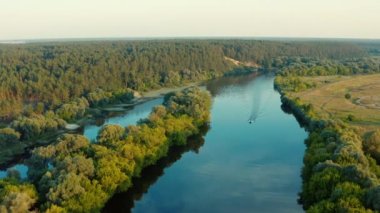 Gün batımında nehri olan güzel bir manzaranın üzerindeki hava manzarası. İnsansız hava aracından gelen hava manzarası güzel bir yaz manzarasının üzerinde uçar. Jet ski nehirde yüzüyor..
