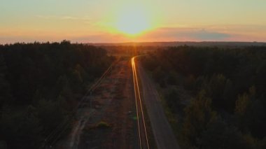 Gün batımı güzelken insansız hava aracı rayların üzerinde uçuyor. Yazın gün doğumunda banliyö demiryolu. Batan güneşin güneş ışınları demiryolu raylarından güzel bir şekilde yansıtılır. Seyahat kavramı.
