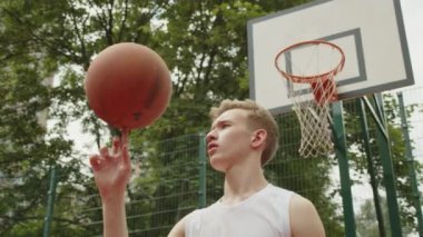 Basketbol sahasında duran ve topu parmağında döndüren bir çocuğun videosu. Genç kızın parmağında dönen bir top ve arkasında bir basketbol sepeti.. 