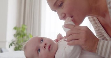 Genç anne aktif oğlunu öpüyor. Sevgi dolu bir anne öpücüğünün yakın çekimi. Anne sağlıklı bebeğin yanağını öpüyor. Anne bebeğine iyi bakıyor. Bebek bakışı. 