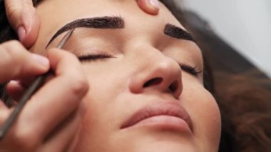Kaş boyası. Güzellik salonunda kadın kaşlarının profesyonel laminasyon prosedürleri. Müşteri yüzü ve stilistin ellerinin çalışmasının yakın görüntüsü. 4K Sinematik Görüntüler.