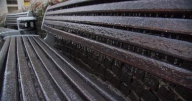 Buz saçakları arasında donmuş şehir bankı. İklim kreması. Buz tutmuş bir bankın yavaş çekim görüntüleri. Kış sonrası soğuk şehir bankı. Doğal afet. Kışın şehir ortamı. 