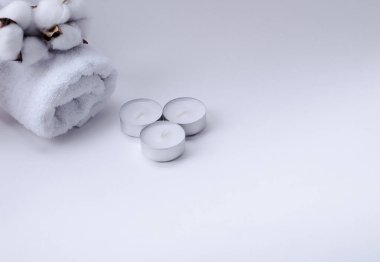 Beyaz, üzerinde pamuk dalı olan terry havlusu ve beyaz arka planda mumlar.