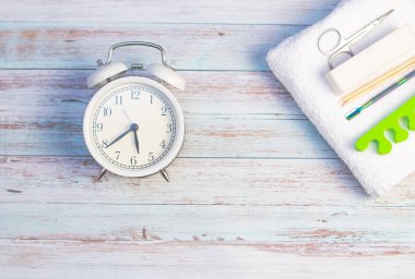 Hafif arka planda beyaz bir çalar saat. Tırnak manikürü için beyaz, terli havlu, makas ve satıcı.