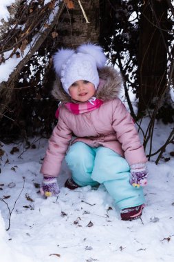 Mavi gözlü, beyaz şapkalı küçük bir kız karda yatıyor.