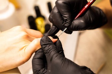 Manikür ustası çalışma aşamasında. Elleri siyah eldivenli, fırçalı, yakın plan.