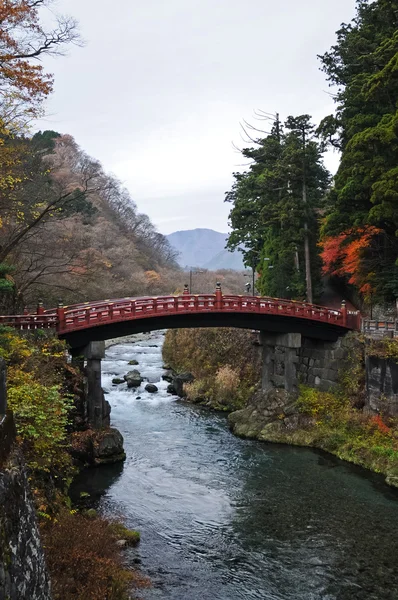Antiguo puente de arco rojo japonés cruzando arroyo rodeado — Foto de Stock