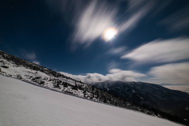 Bulutlu bir gecede kayak merkezinde kayak pistinde taze kar. Dağ kayak pistinde kar temizleyici izleri var..